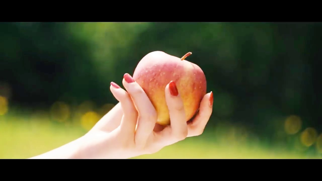 a hand holding an apple in bright daylight, with an outside grass setting blurred in the background.