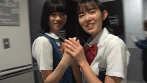 beyooooonds members kobayashi honoka and takase kurumi - they're holding hands with some weird undecipherable item between them, they smile at the camera when it comes by